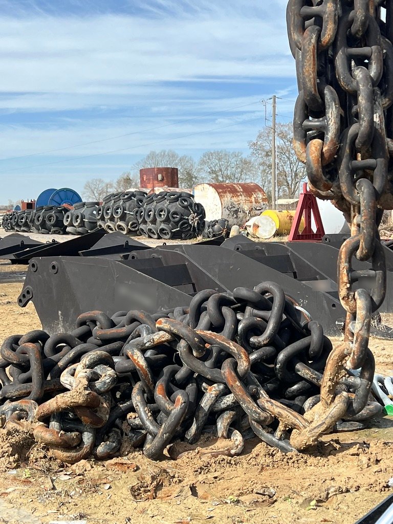 Pile of large anchor chain with black anchors behind it in the Wet Tech yard
