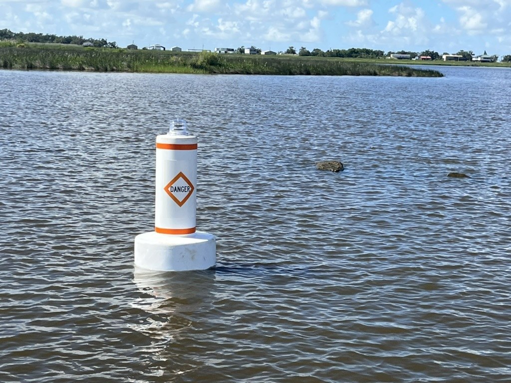 M-711LP 28 inch marker buoy (700 mm class), white with orange bands and danger diamond, on station in shallow marsh water