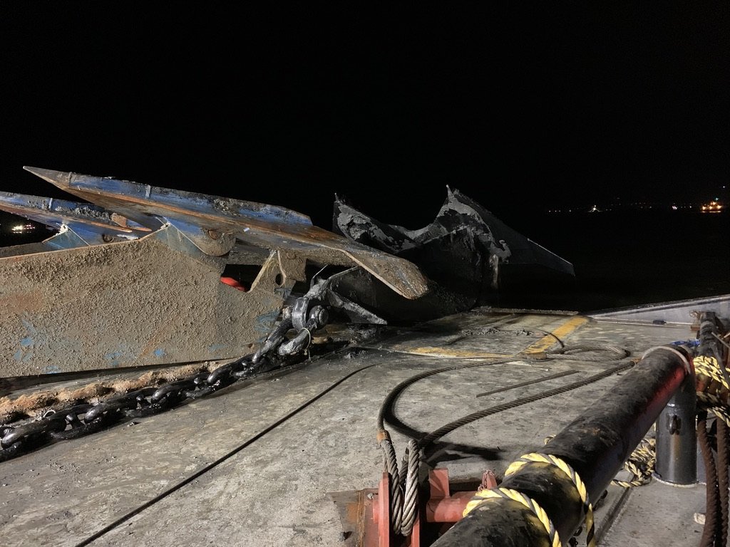 Two large blue and black fluke anchors with chain on a barge deck at night