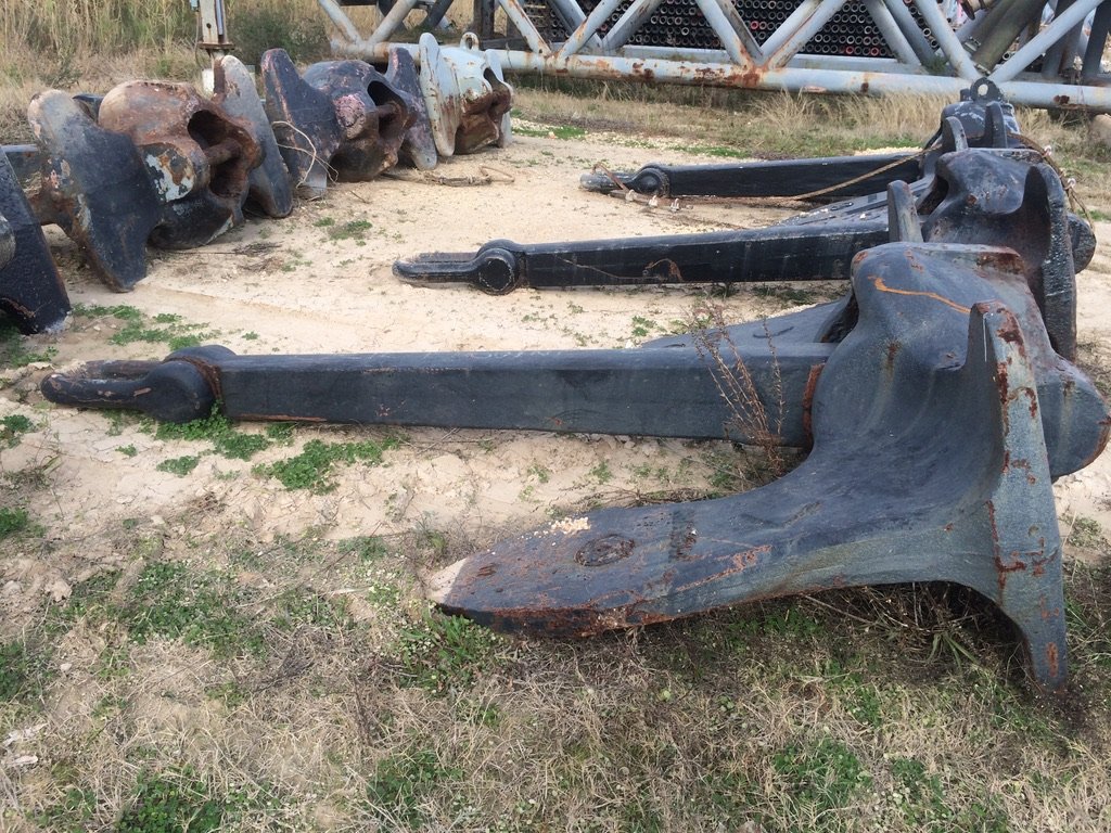 Row of large weathered black fluke anchors lying on sandy ground in the yard