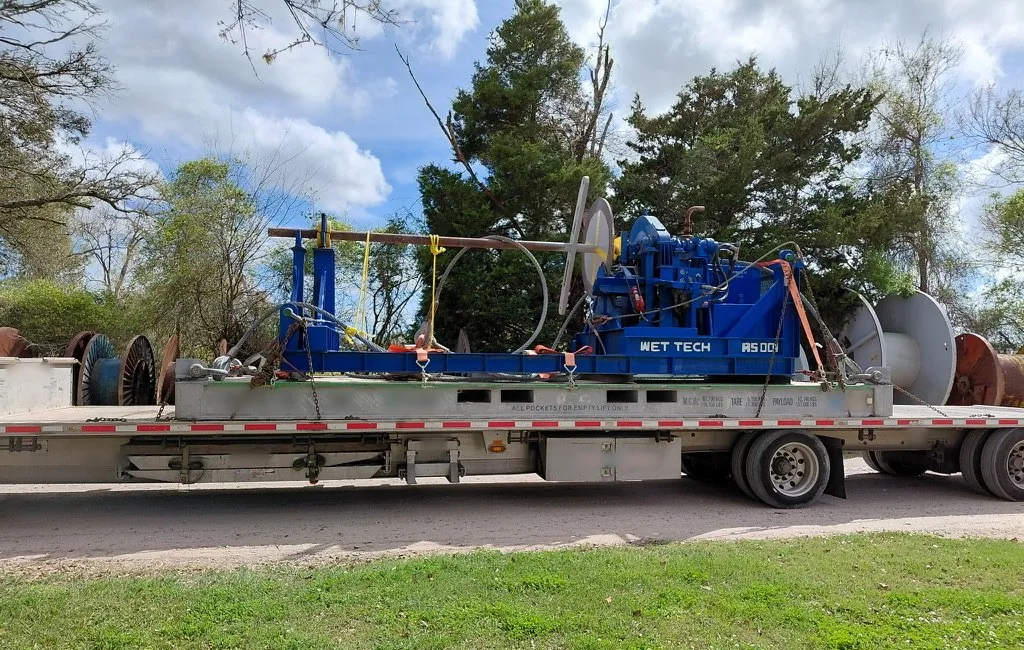 Side view of the Wet Tech RS-001 spooling unit strapped to an offshore shipping flat rack on a flatbed trailer