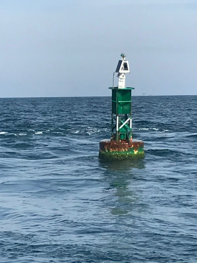 Green steel BL 620 lighted sound buoy on station at sea, with a solar panel and light on top of its tower